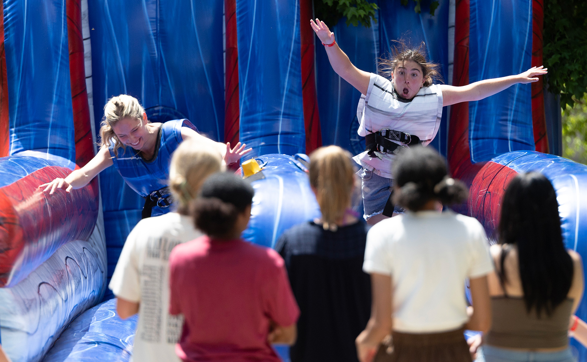 Two women competing on a bungee run obstacle in front of a small group of observers. 