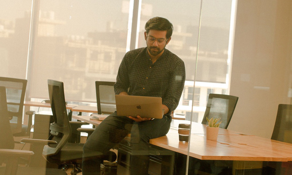 Archit sitting on conference table with computer and coffee