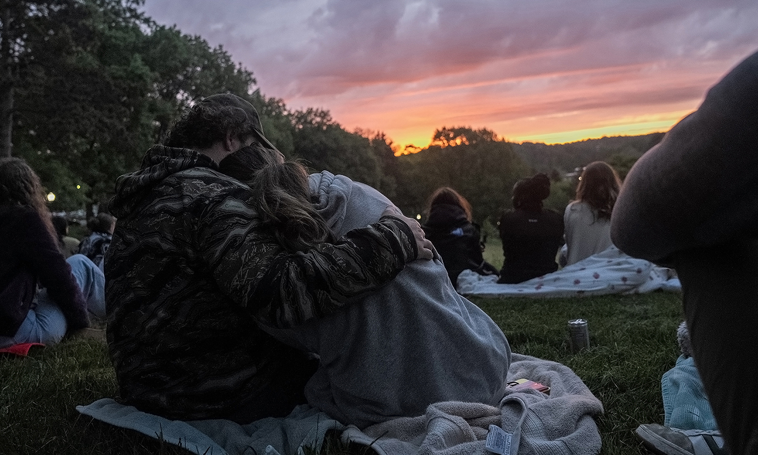 Two students snuggling as the sun rises in the sky stretched out in front of them.