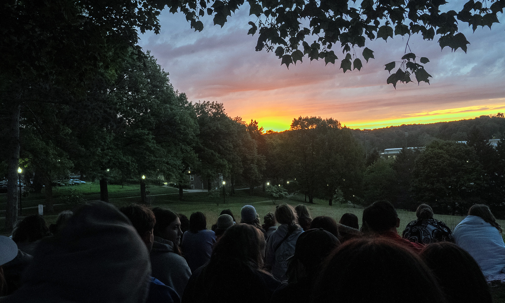 A group of students sitting on grass and watching the sun rise over the horizon. 