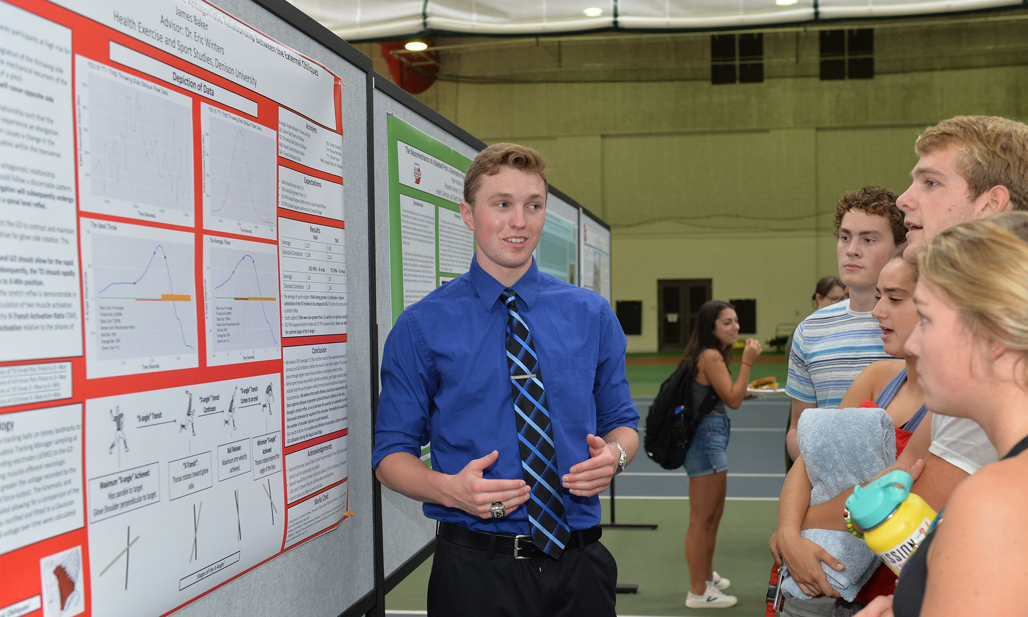 James Baker stands in front of a poster and talks to students about his research project