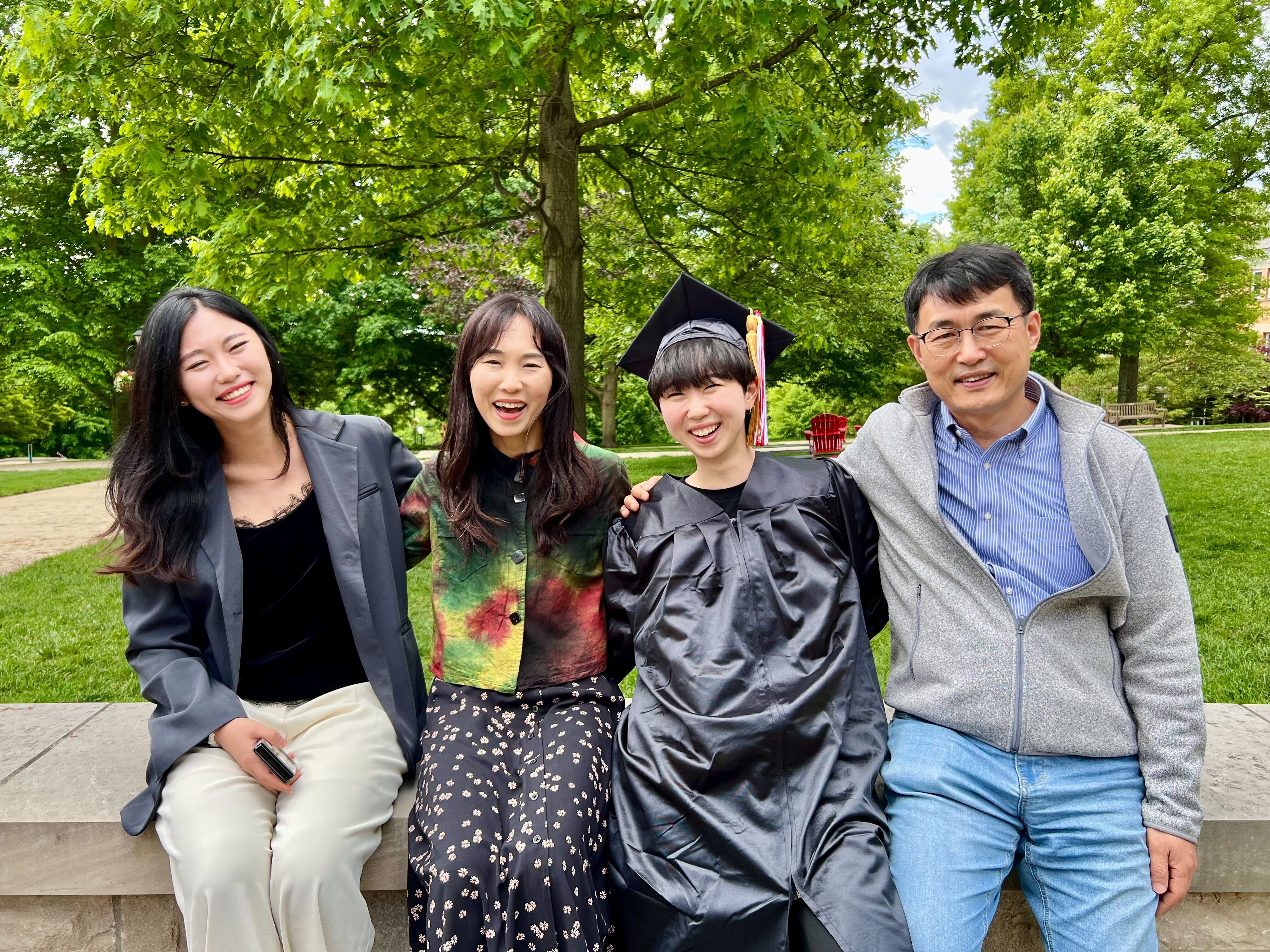 The Kim family -- four people sitting on a concrete wall outside at Denison University. 