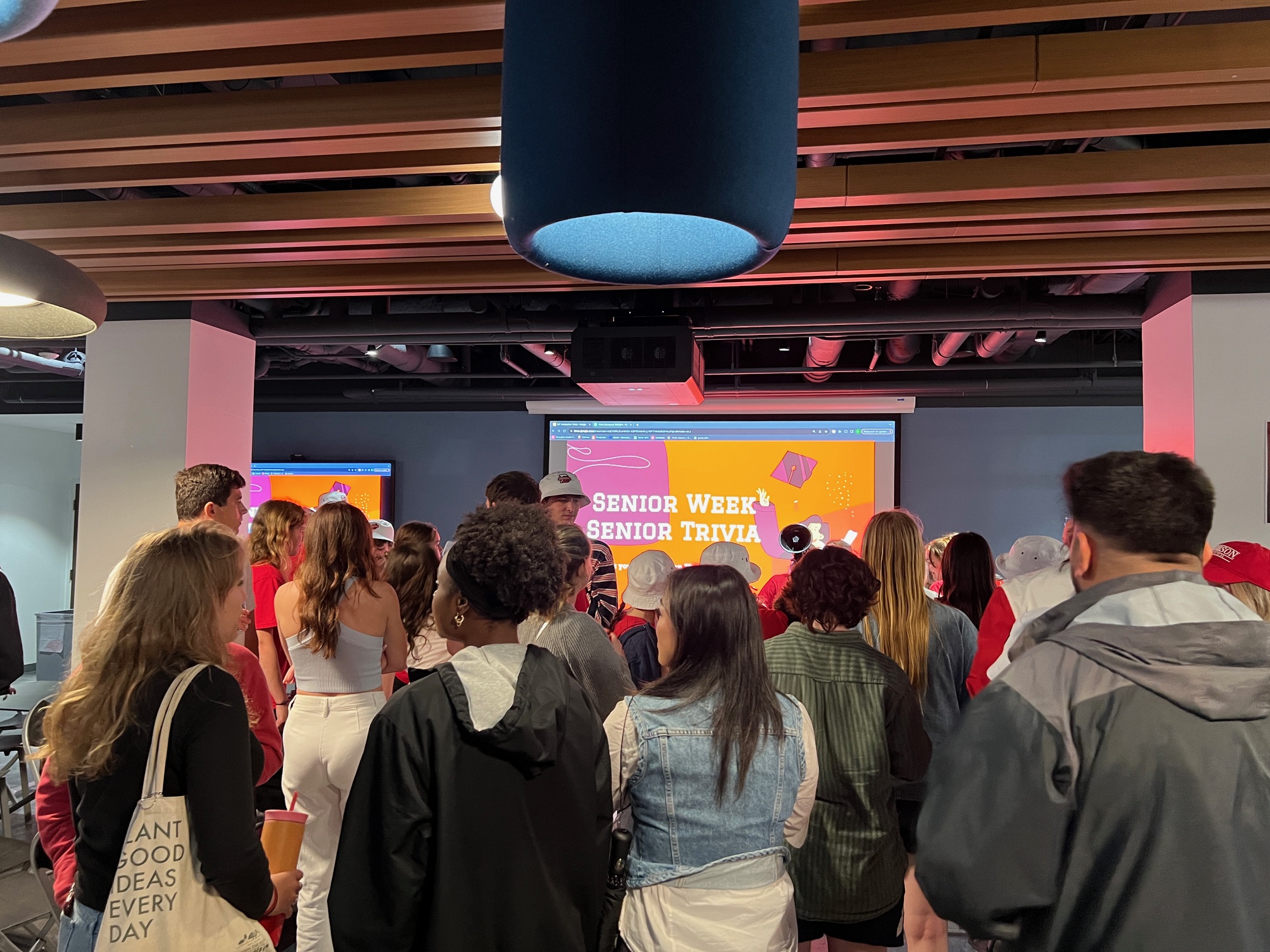 Group of people standing in a room in front of a screen that says "senior week senior trivia."