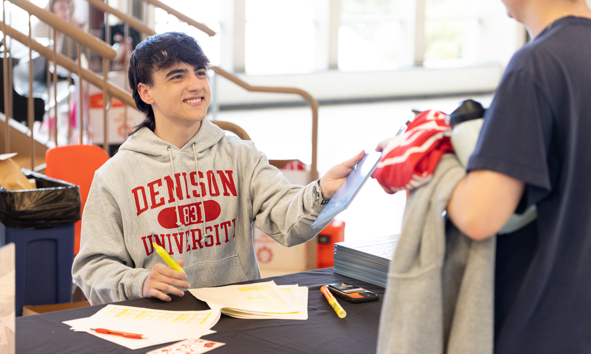 A student in a Denison sweatshirt handing out a yearbook.