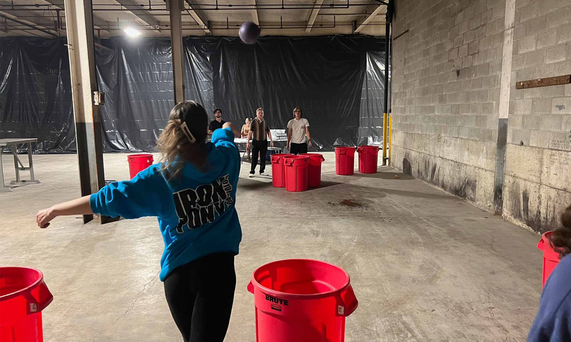 Woman throwing a ball across a room into a garbage can.