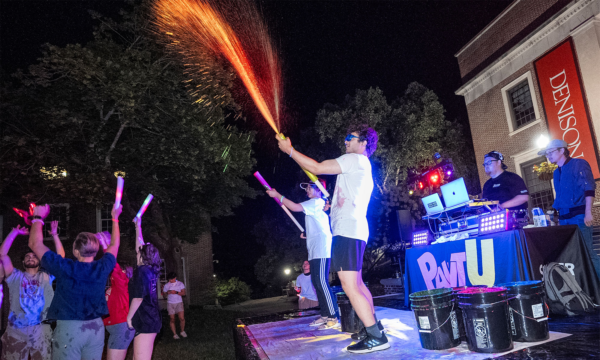 Two people on a stage launching streams of paint into a crowd