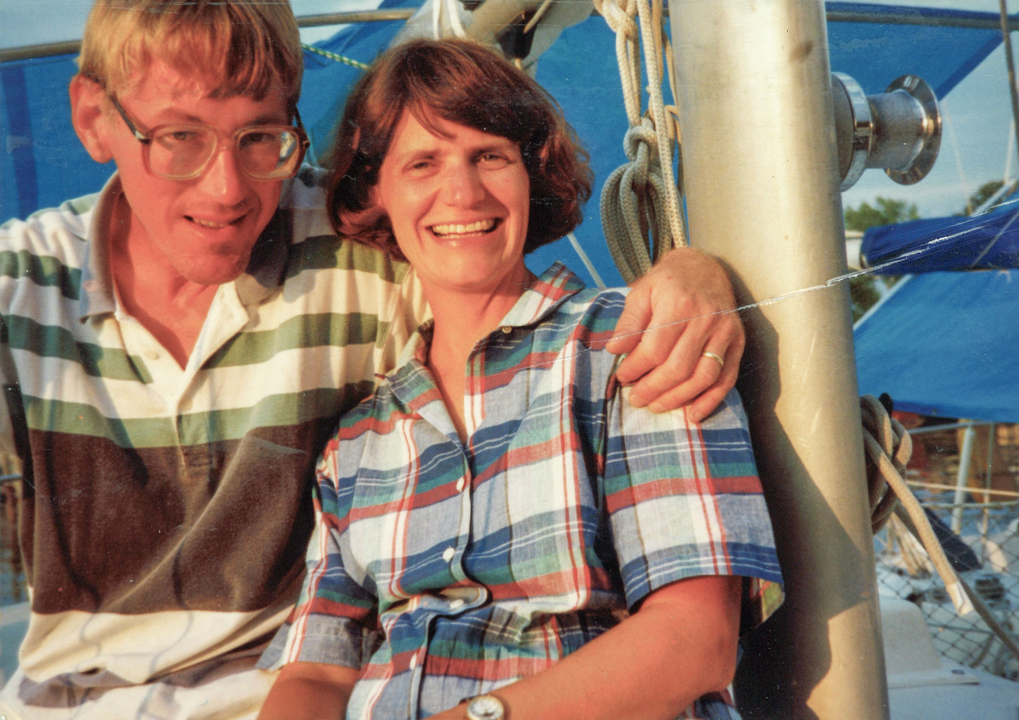 A man and a woman on a sailboat. His arm is around her.