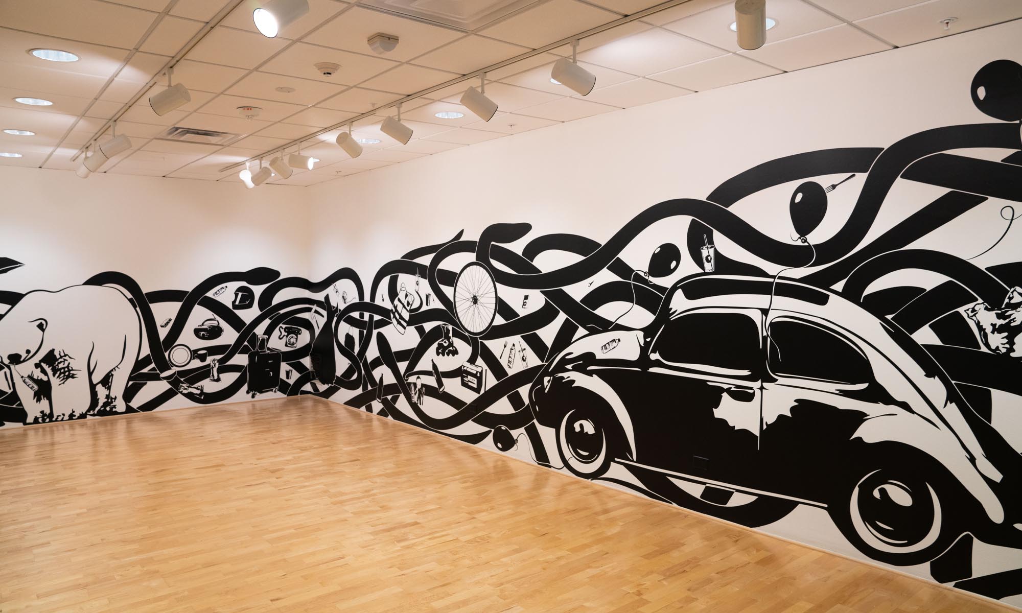 Wall mural comprised of black snake-like lines intersecting around the room wrapping around a two-dimensional image of a car.