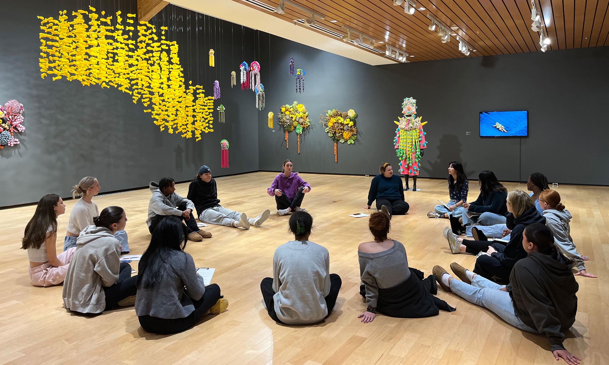 A group of students sit in a circle amid an exhibit at the museum.