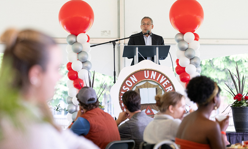 President Adam Weinberg standing at a lectern surrounded by balloons and speaking to an audience. 