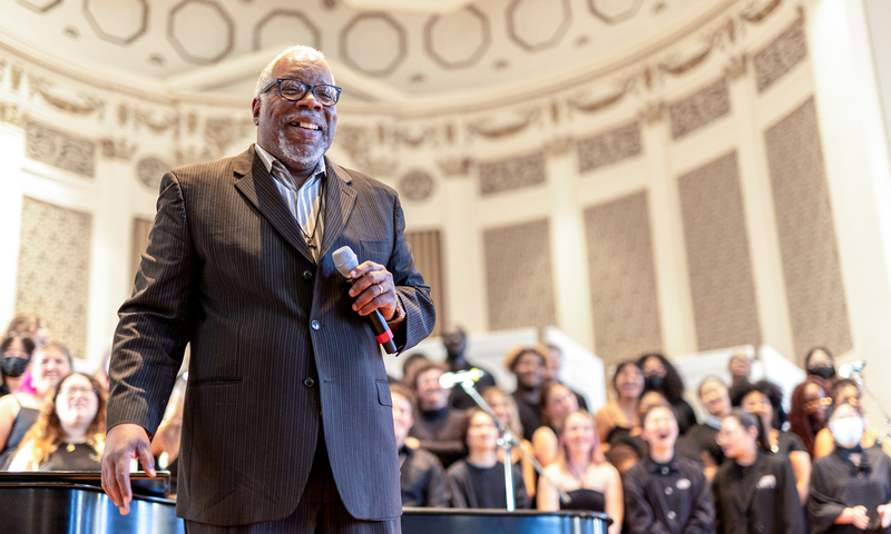 Timothy Carpenter on stage inside Swasey chapel with singers behind him