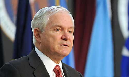 Robert Gates speaks with colorful flags in the background