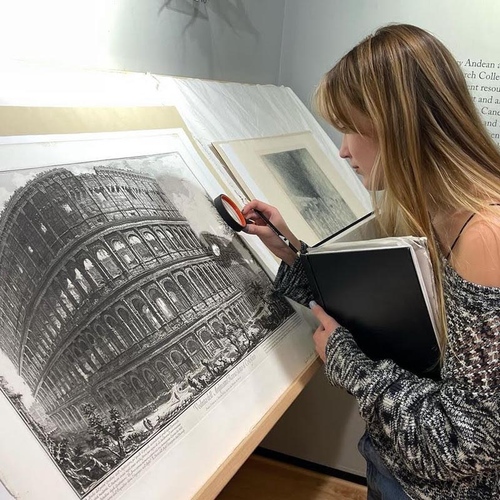 A student uses a magnifying glass to observe details on an illustrated print.