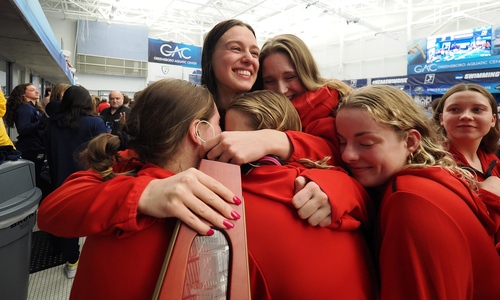 Denison swimmers embrace senior co-captain Tara Culibrk clutching a trophy.