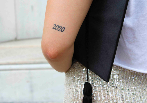 Student holding a graduation cap with a '2020' tattoo on their arm