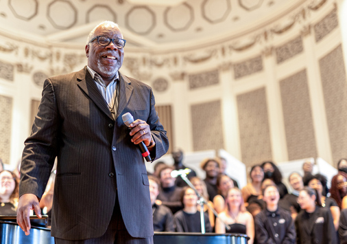 Timothy Carpenter on stage inside Swasey chapel with singers behind him