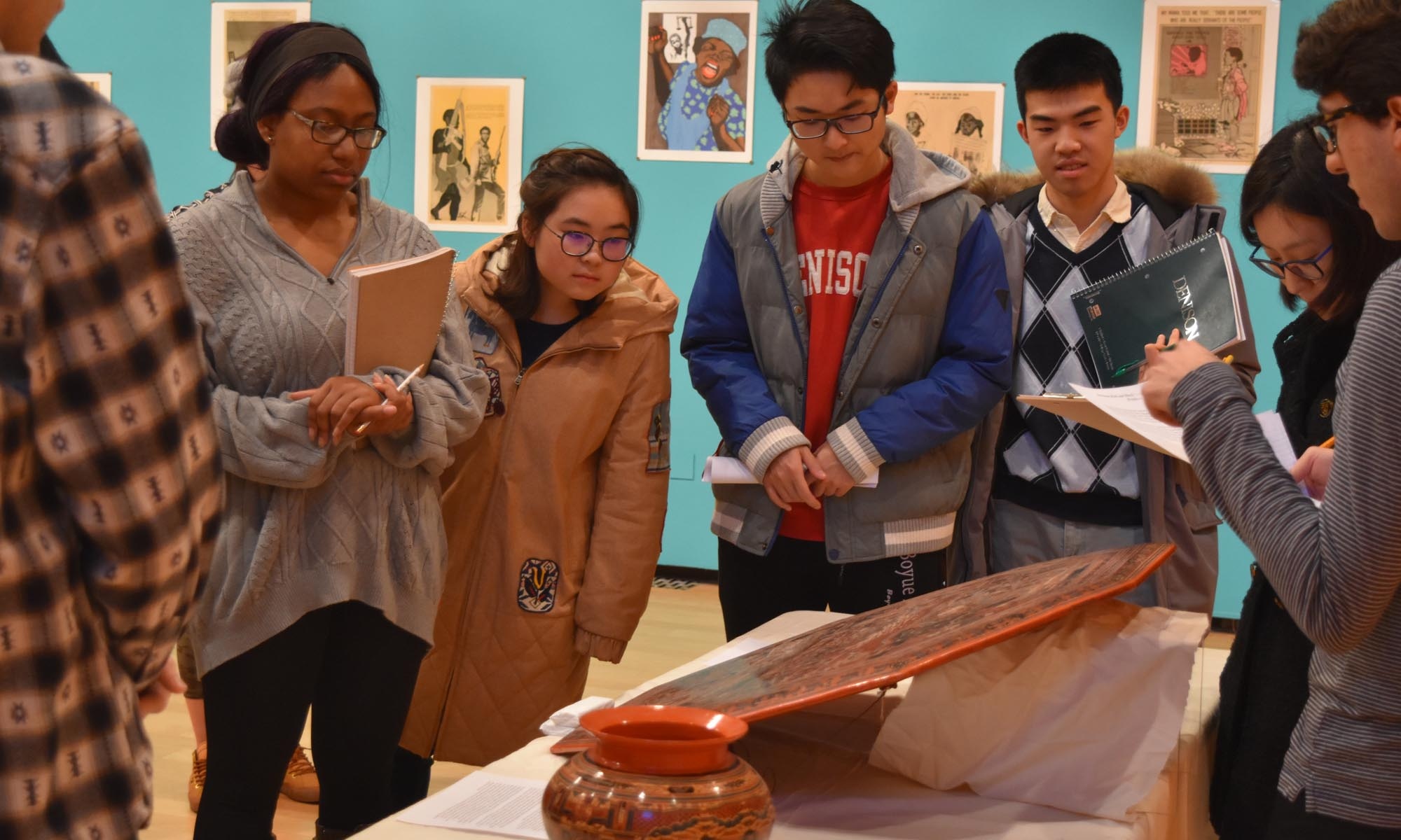 Students gather around an exhibition piece taking notes during a class.