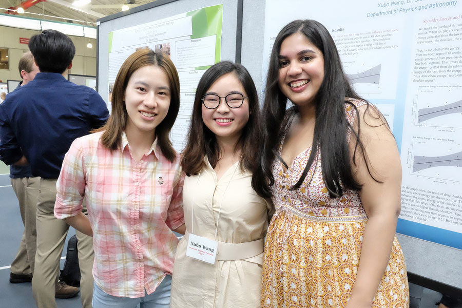 Three students pose in front of poster