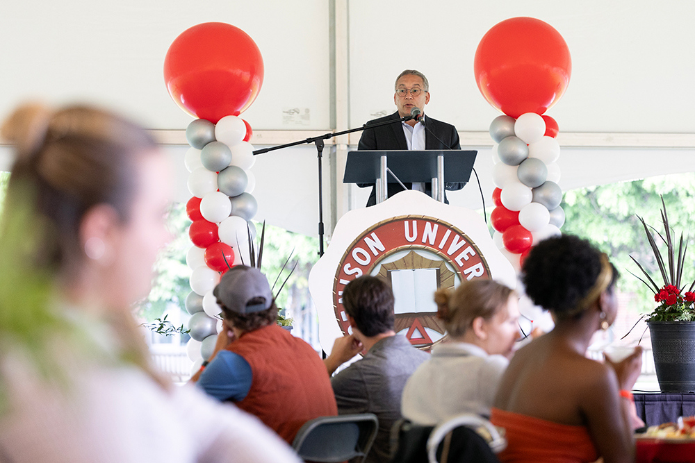 President Adam Weinberg standing at a lectern surrounded by balloons and speaking to an audience. 