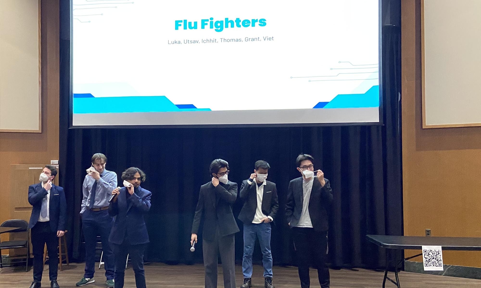 Six students billing themselves as the “Flu Fighters” stand on the Herrick Hall stage in white medical masks.